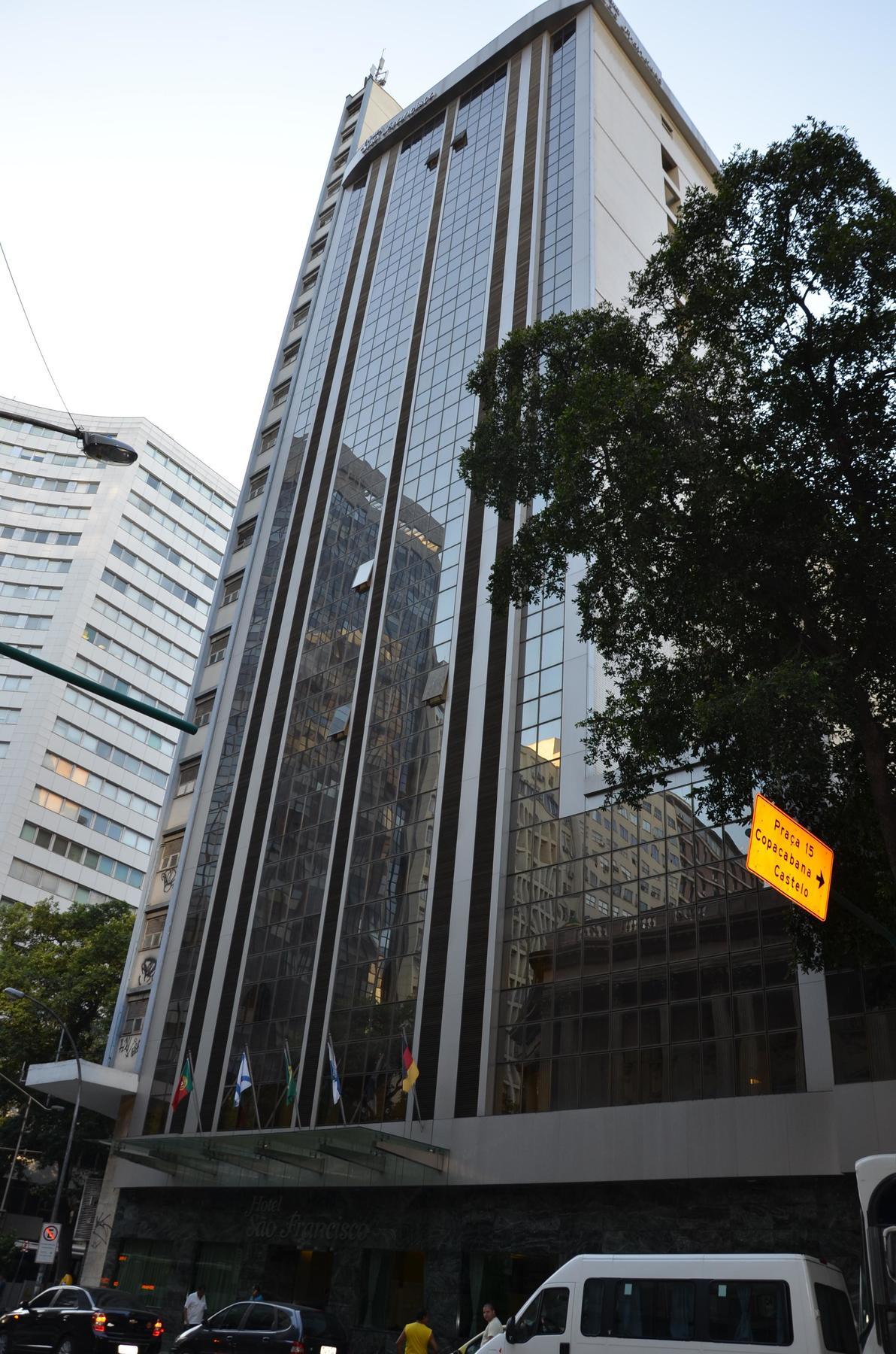 Hotel Atlantico Tower Rio de Janeiro Exteriér fotografie The photo shows a city street with tall buildings. In the foreground, there is a modern glass skyscraper featuring reflective surfaces and vertical lines. Next to it, there's another building with a different architectural style, also made of glass. 